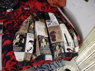 This item is a 2Pac Shakur patchwork leather jacket, featuring a black, white, and gold newspaper print design.