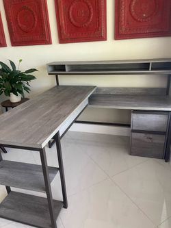 Gray L shaped desk with filing cabinet, phone charger,  and metal framework