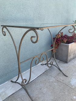 Vintage wrought iron console table with glass top and scrolling details.