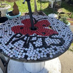 Rustic shabby outdoor spool wood table with bottle cap nailed on top- 39.5 inches wide/ 32 inches high holds umbrella in middle  - umbrella not includ