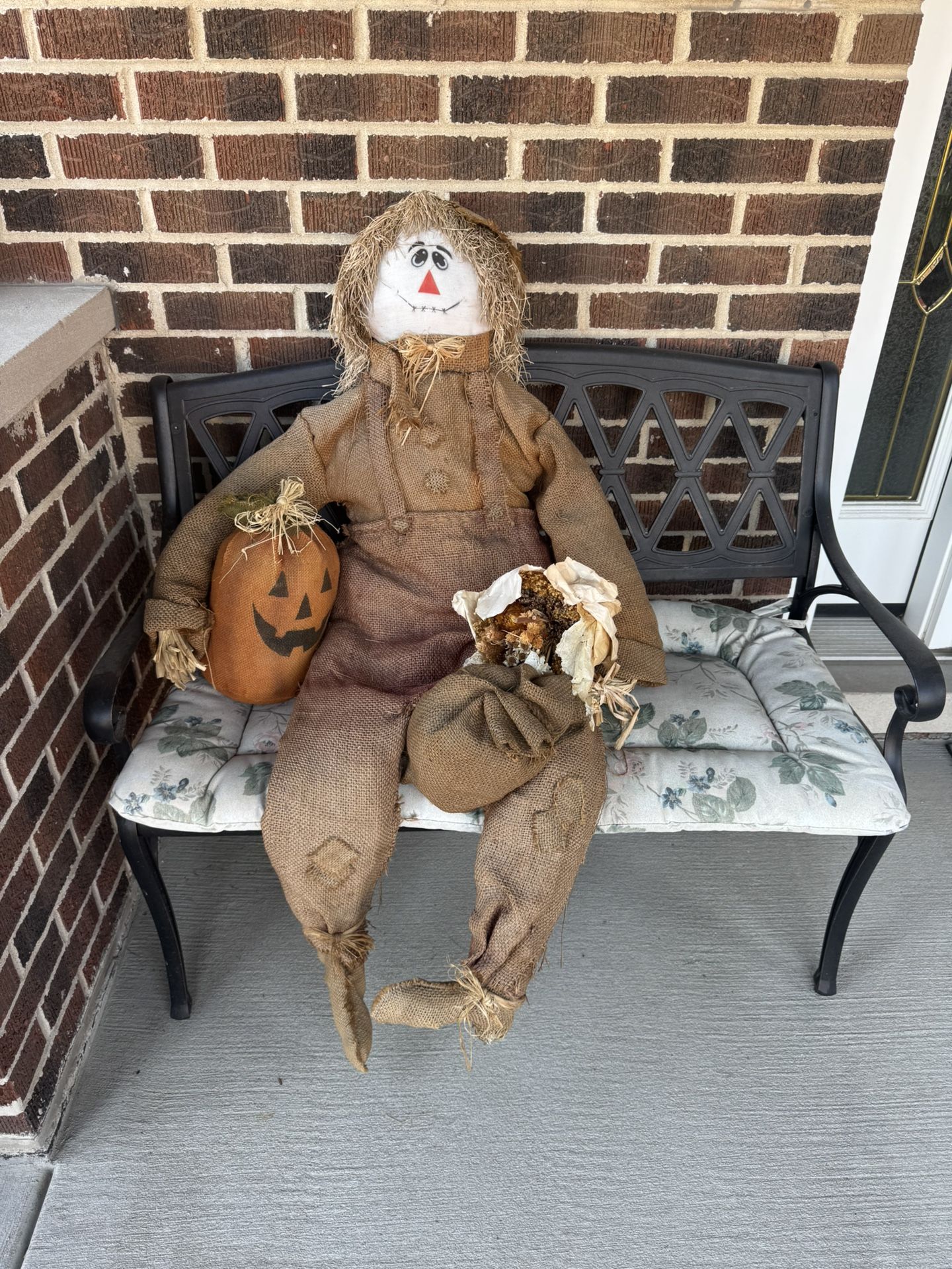 Autumn decor - sitting straw man holding pumpkin and dried flowers