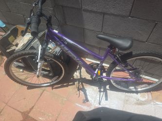 The bike in the image is a Huffy Highland 24" Mountain Bike in purple. This model features a steel frame, twist shifters, and a 15-to-21 speed drivetr