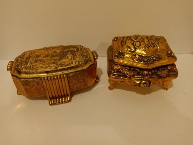 Two ornate gold metal trinket box with engraved scenes. One is 3 1/2” wide and the other is 4 1/2” wide. Red velvet lining. 