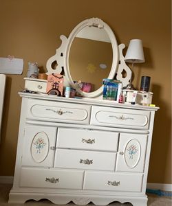 Elegant white dresser with floral details and attached mirror.