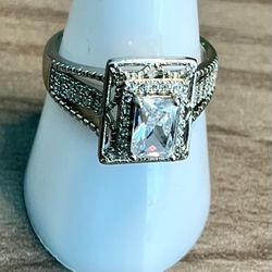 Elegant silver-tone ring featuring a white emerald-cut cubic zirconia center. Sparkling pavé accents add refined brilliance. A versatile, polished des