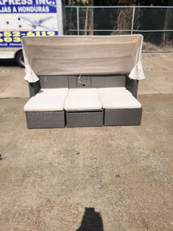 Beautiful modern outdoor wicker patio daybed/lounge set with adjustable canopy, convertible seating layout, matching ottomans, and lift-top table/stor