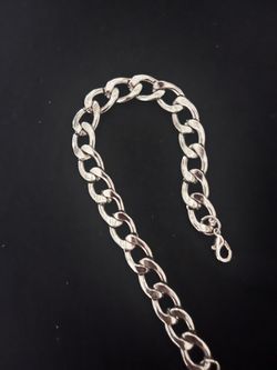 Polished silver-toned curb chain bracelet has a lobster claw clasp. The material is a metallic silver color with flat, interlocking links.