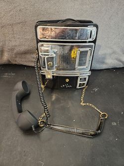 This unique piece is a novelty telephone-shaped crossbody bag, designed to resemble a vintage payphone. It features a decorative handset, a simulated 