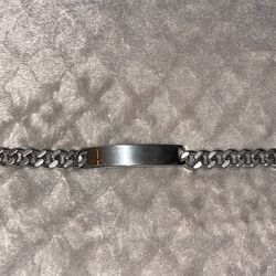 Cuban link ID bracelet featuring a polished silver curb chain and a centered, engravable ID plate with a gold-tone cross emblem.