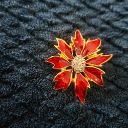 vintage gold-tone poinsettia brooch features vibrant red enamel petals and a sparkling rhinestone center.
