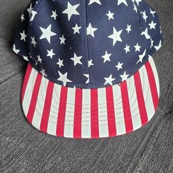 Patriotic snapback hat has navy blue crown with white stars and red and white striped brim. This one size fits all cap is made of cotton and features 