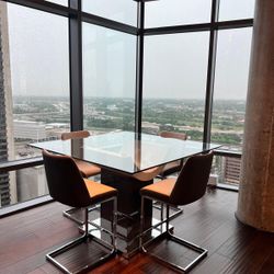 Glass dining table with 6 tall gray chairs.