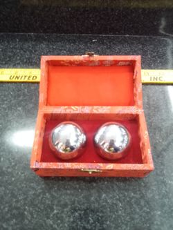 The image shows a pair of Chinese Baoding balls (also known as meditation, stress, or hand exercise balls) resting inside a decorative red cushioned b
