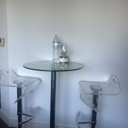 Glass round high top table with swivel adjustable modern acrylic bar stool chairs.