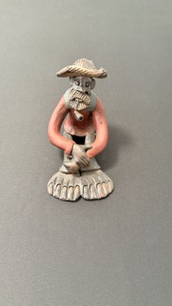 A bearded man sitting, smoking a pipe.