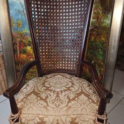 Vintage Hollywood Regency Tall Cane Back Fireside Lounge chair. Brown wooden chair with rattan backing. Golden tassels hanging from the front legs. 