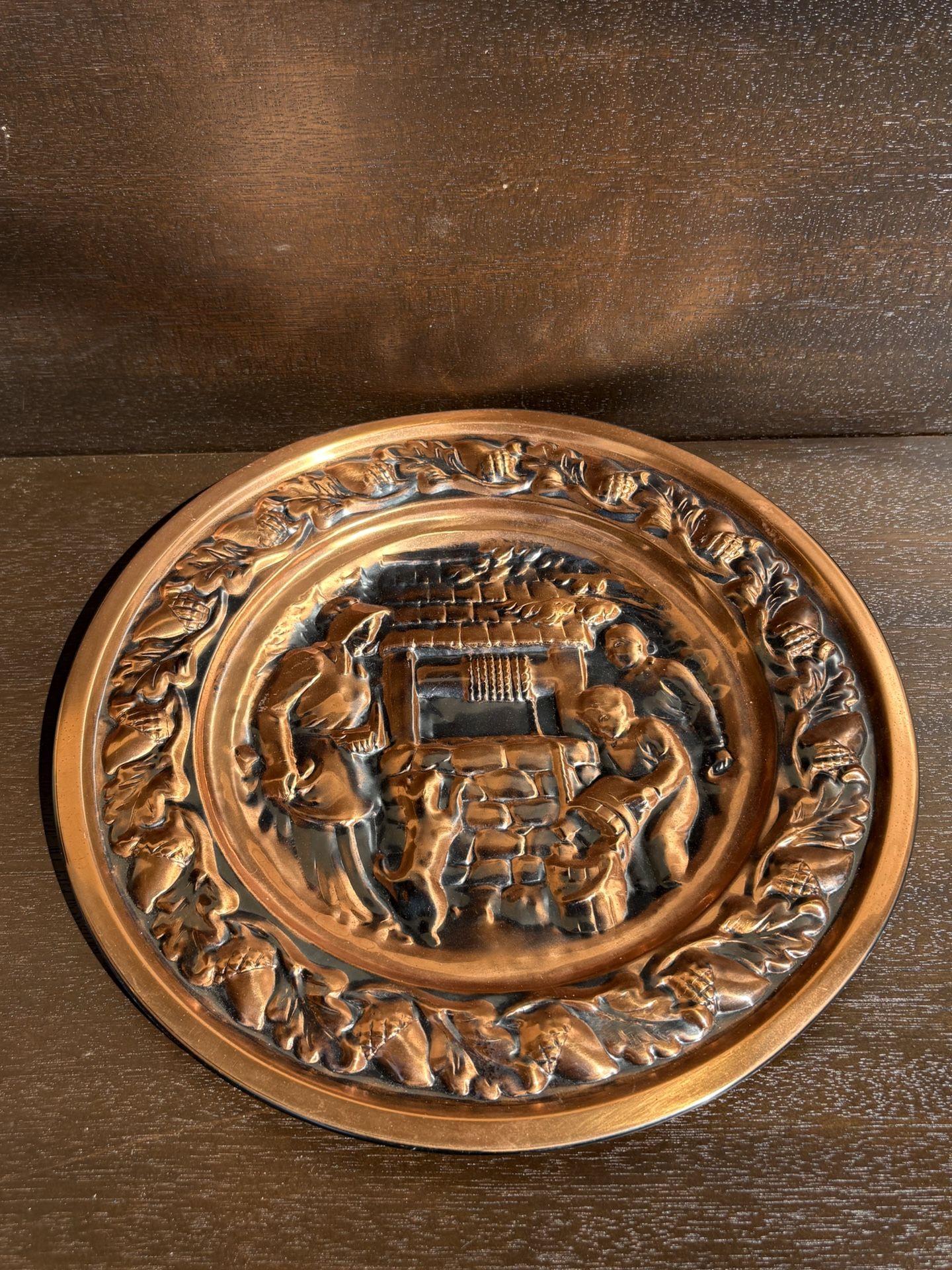 This is a vintage copper wall plate, often referred to as "Family at the Well" or "Family at the Well