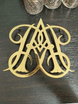 It is a solid brass vintage trivet featuring the monogram or cipher of Queen Anne.