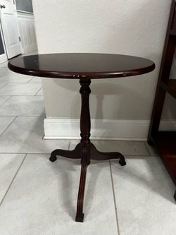 tilt-top side table featuring a reddish-brown wood finish and a sturdy pedestal base.