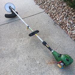 Massive cutting power. Gas-powered John Deere brush cutter has a green engine housing and a silver metal shaft. This tool is equipped with a circular
