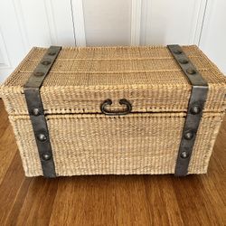 Handwoven rattan storage trunk with steel frame on wheels.