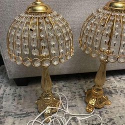 pair of gold and crystal table lamps, likely in a vintage or French Empire style. The design features a gilded metal base and a shade constructed of a