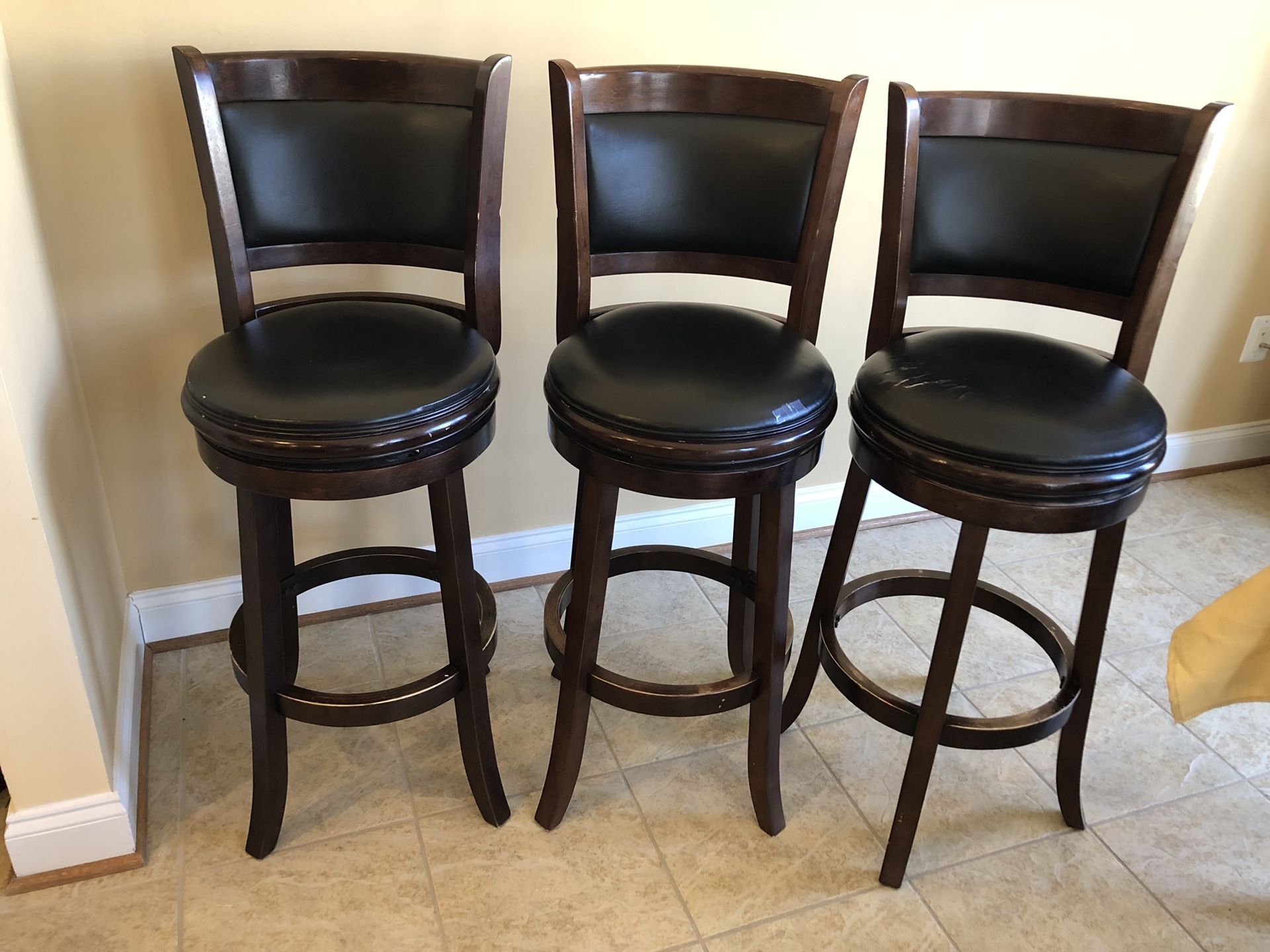 Three brown wooden frame black leather padded bar stools