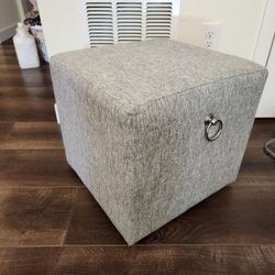 gray linen fabric ottoman with white plastic caster wheels and 2 metal rings, clean and great condition 