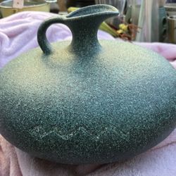 large, round, green pottery vase with a textured surface and a small spout. It Has a incised zigzag patter Of A Snake
