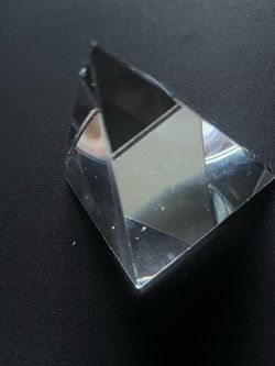 Clear glass optical prism has a pyramid shape. This decorative piece is made of solid glass and reflects light through its faceted surfaces. It has a 