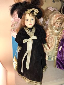 Beautiful porcelain doll. With light brown hair and blue eyes. She’s wearing a beautiful dress, hat with a purse too. Comes with doll stand. In good