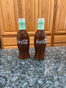 Coke Coca Cola Mini Ceramic Bottle Shaped Pair of Salt and Pepper Shakers.  Size approximately 5 inches tall.  Preowned never used.  Has been on displ