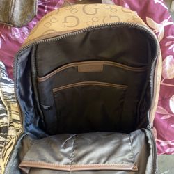 This is a GUESS backpack (tan/brown), made of faux leather with the all-over “G” monogram and the triangle GUESS logo on the front.