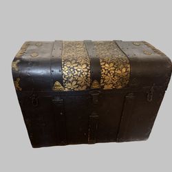 Antique camelback steamer trunk with gilded leaf motif and metal hardware.