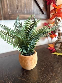 compact artificial fern featuring textured green fronds set inside a bulbous, natural wood-finish pot.