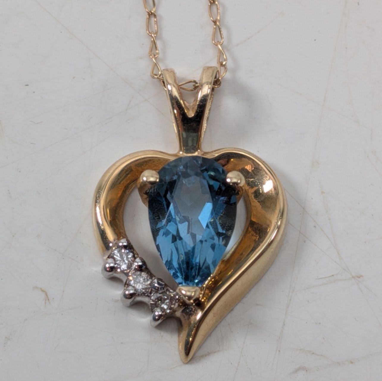 14K Yellow Gold Heart Necklace β Elegant 14K yellow gold heart pendant featuring one vibrant blue stone and three sparkling clear stone accents. Marke