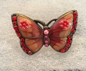 Vintage style butterfly brooch pin. Features warm peach/pink enamel wings lined with sparkling ruby red rhinestones and pink bead details on a brass/a