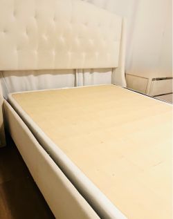 Queen bed frame with a tall button-tufted headboard in cream/ivory fabric. Wingback-style side panels and a solid wood slat platform — no box spring n