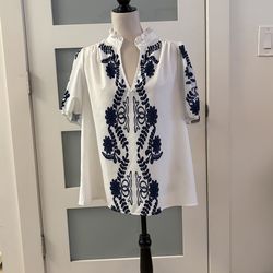 This white blouse with navy blue floral print is a popular style available at various women's fashion stores. It features a mandarin collar with ruffl