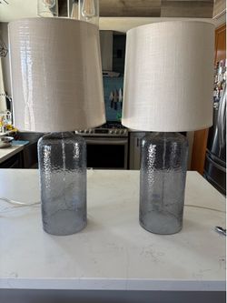 Beautiful matching set of two modern table lamps with textured smoked glass bases and neutral linen-style drum shades.