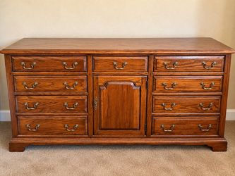 traditional oak-style 8-drawer dresser with a center storage cabinet and decorative brass-style handles.