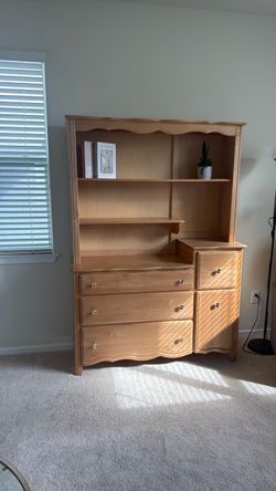 Light wood dresser with an upper shelving unit featuring decor.