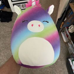 Squishmallows plush toy, likely Clarissa the Rainbow Unicorn.  Brand: Kellytoy / Jazwares.  Appearance: Diagonal rainbow stripes with a white belly, w