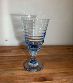 It is a blue Libbey wine or water glass from the "Sirrus" collection, characterized by its ribbed design and solid-stem base.