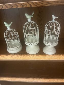 ($10.00 Each) Decorative metal birdcage set includes three pieces of varying heights. Each piece is off-white with a distressed finish and a bird figu