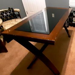 rectangular wooden table with a black glass inlay top and X-shaped legs.