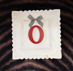 Monogram plaque with red capital letter "O” accented with a gingham fabric  black-and-white checkered bow.