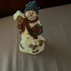 Snowman figurine holding a wreath and a birdhouse