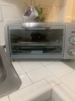 Silver Black + Decker toaster oven has a front glass door and manual dial controls for temperature and titme settings. This appliance includes an inte