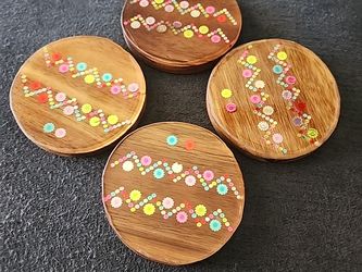 Set of 4 round wooden coasters featuring colorful hand-painted floral and dot patterns. Each coaster has a natural wood-grain background with bright p